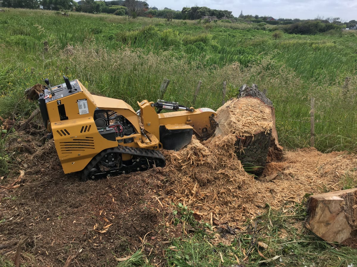 Tracked grinder working through a large stump beside a rural fence